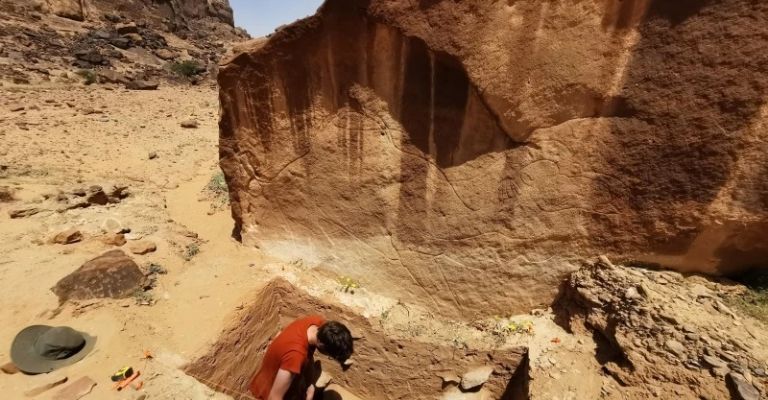 Esta imagen, proporcionada por el Proyecto de Arte Rupestre y Arqueología de Sahout, muestra a expertos excavando el suelo bajo la roca tallada de un animal, en un desierto del norte de Arabia Saudita en 2023. (Maria Guagnin/Proyecto de Arte Rupestre y Arqueología de Sahout vía AP)